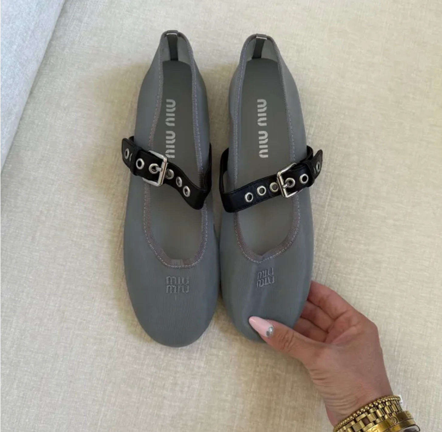 Gray shoes with black buckles held by a hand on a beige surface