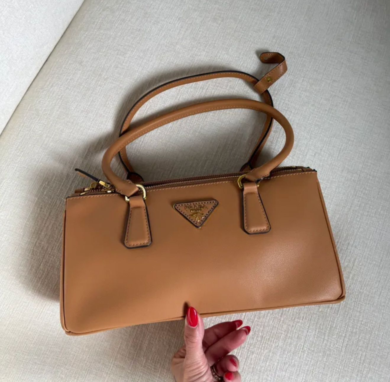 Brown handbag with a visible brand logo held by a hand on a light background